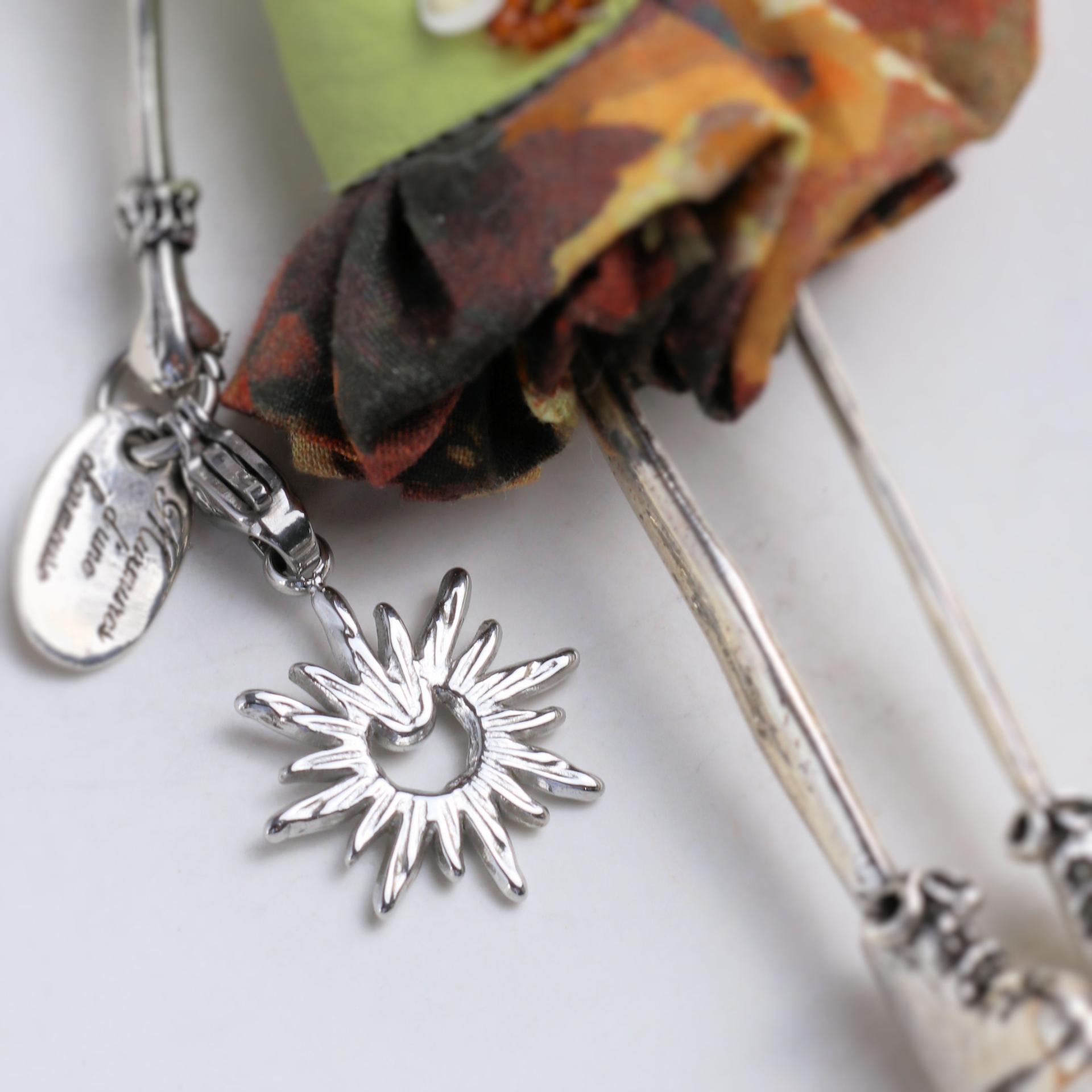 Breloque soleil ajouré ornée d'un petit zircon, tenue par la poupée de ce collier vert femme fait main.