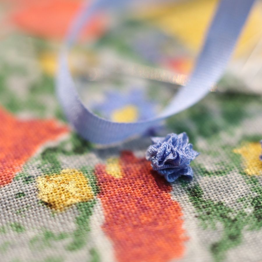 Zoom sur la broderie d'art miniature d'une éclosion de fleurs en ruban de soie sur la robe d'un pendentif poupée talisman unique Murmures d'une charmeuse